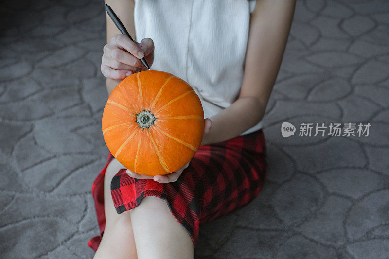 Asian Woman Drawing on a Pumpkin to Make a Jack O'Lantern